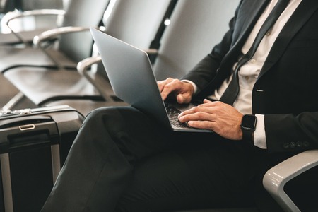 Close up of businessman dressed in suit using laptop computer while sitting at the airport lobbyの写真素材