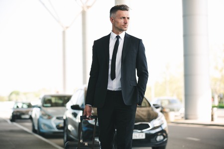 Handsome mature businessman catching a taxi while walking outside the airport with a suitcaseの写真素材