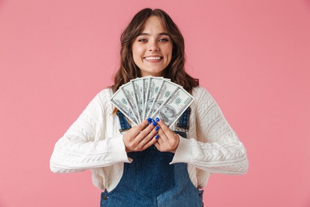 Portrait of a cheerful young girl holding money banknotes isolated over pink backgroundの写真素材