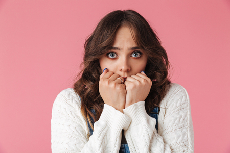 Worried brunette woman in casual clothes covering her mouth and looking at the camera over pink backgroundの写真素材