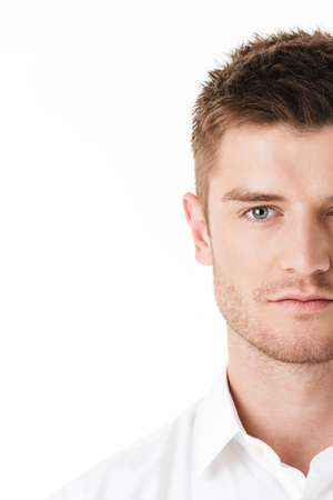 Cropped image of a serious young man's face looking at camera isolated over white backgroundの写真素材
