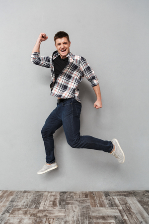Full length portrait of a happy young man jumping over gray backgroundの写真素材