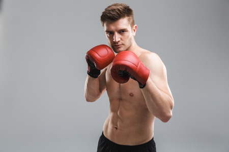 Portrait of a strong shirtless sportsman wearing boxing gloves isolated over gray backgroundの写真素材