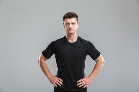 Portrait of a focused young sportsman standing with arms on hips isolated over gray backgroundの写真素材
