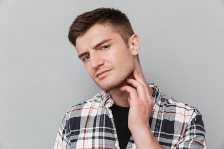 Portrait of a concerned young man in plaid shirt touching his face over gray backgroundの写真素材