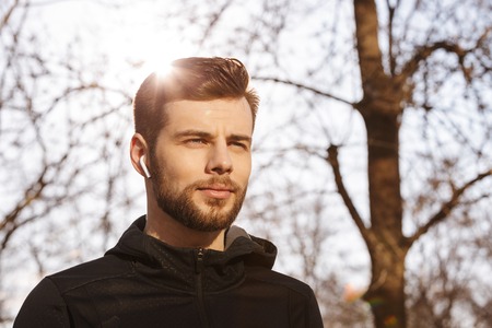 Close up of a handsome young sportsman in earphones looking away outdoors