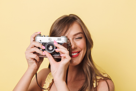 Close up portrait of a smiling young girl taking picture with a photo camera isolated over yellow backgroundの写真素材
