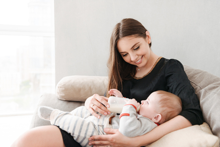 Image of happy young family. Mother feeds her little child indoors at home.の写真素材