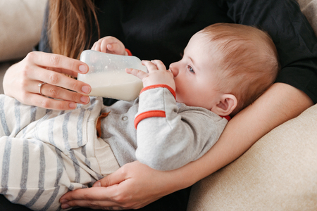 Cropped photo of young family. Mother feeds her little child indoors at home.の写真素材