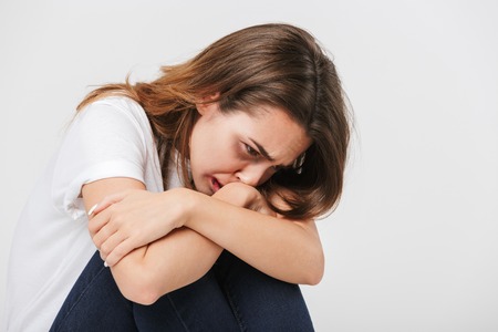 Abused scared woman with wounds on her face sitting and crying isolated over white backgroundの写真素材
