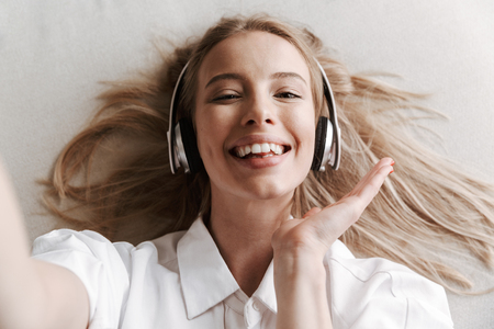 Top view of excited young woman in headphones taking a selfie while listening to music on a couchの写真素材