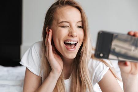 Photo of cute beautiful young woman indoors at home make selfie by mobile phone winking.の写真素材