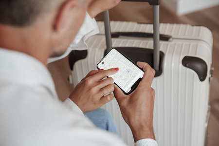 Cropped photo from above of man and woman in casual clothing checking location using map in smartphone while staying at hotel room with luggage. Holiday or vacation conceptの写真素材