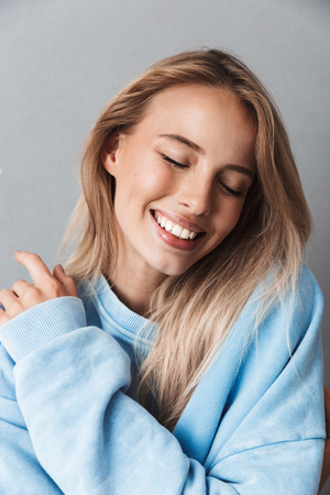 Close up of a smiling young girl in blue sweatshirt with eyes closed isolated over gray backgroundの写真素材