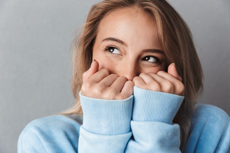 Close up of a lovely young girl in blue sweatshirt looking away isolated over gray backgroundの写真素材