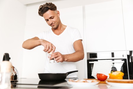 Handsome man cooking eggs for breakfast while standing at a kitchenの写真素材