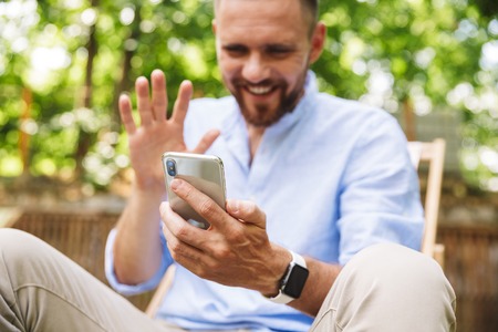 Photo of happy young bearded man outdoors talking by mobile phone waving.の写真素材