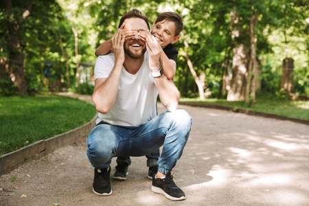 Image of happy little son covering eyes of his cheerful father have fun outdoors in park nature.の写真素材