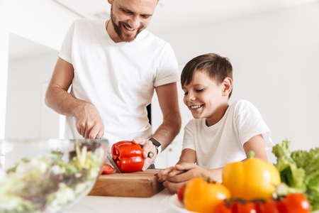 Photo of cheerful young man father dad cooking with his son indoors at home in kitchen.の写真素材