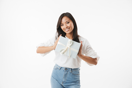 Image of happy birthday asian girl 20s smiling and holding present box in hands isolated over white backgroundの写真素材
