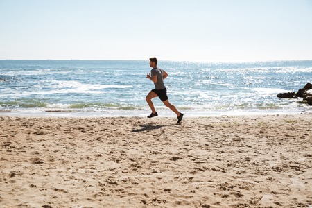 Strong young sportsman jogging on a sandの写真素材