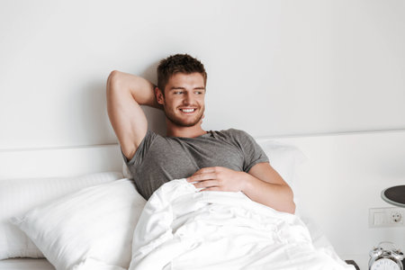 Attractive young man sitting in bed at homeの写真素材