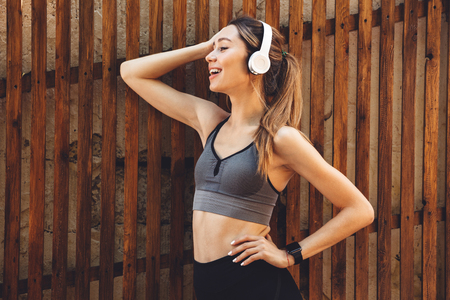 Portrait of a smiling young fitness girl listening to music through wireless headphones outdoorsの写真素材