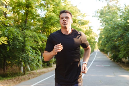 Confident young shirtless sportsman in earphones running at the road outdoors