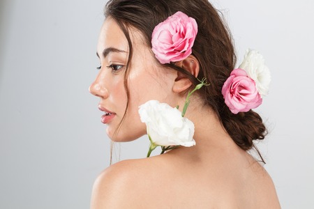 Side view beauty portrait of a pretty young topless woman with make-up posing with eustoma flowers at her face isolated over gray backgroundの写真素材