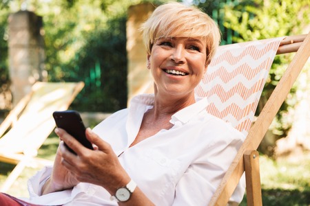 Happy mature woman using mobile phone while resting at the park