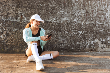 Image of strong young sports woman outdoors on the beach using mobile phone.の写真素材