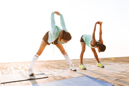 Photo of strong young two sports women friends outdoors on the beach make sport exercises.の写真素材