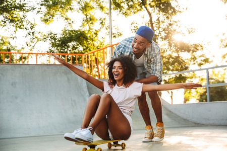 Portrait of a happy young african couple with skateboards having fun together at the skate parkの写真素材