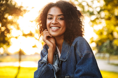 Delighted young african girl in denim jacket spending good time at the parkの写真素材
