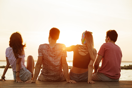 Back view photo of group of four friends loving couples walking outdoors on the beach.の写真素材