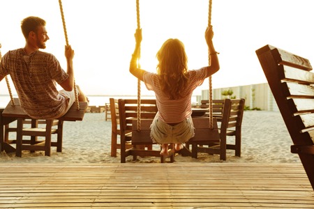 Back view photo of friends outdoors on the beach riding on swing.の写真素材