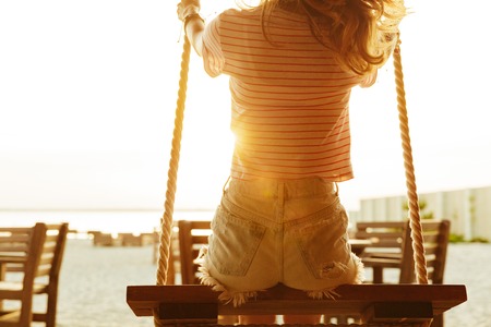Back view image of young lady outdoors on the beach riding on swing.の写真素材
