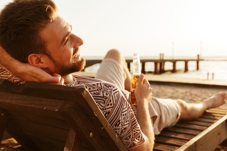 Picture of handsome man have a rest outdoors on the beach drinking beer.の写真素材