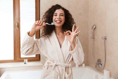 Photo of emotional beautiful young cute woman in bathroom brushing cleaning her teeth.の写真素材