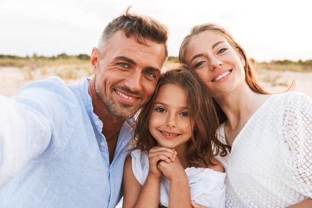 Image of young happy family outdoors at the beach take a selfie by camera.の写真素材
