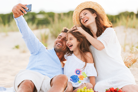 Image of young cute happy family having fun together outdoors at the beach make selfie by mobile phone.の写真素材