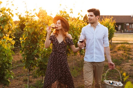 Photo of young cute happy loving couple outdoors drinking wine holding basket with bottles.の写真素材