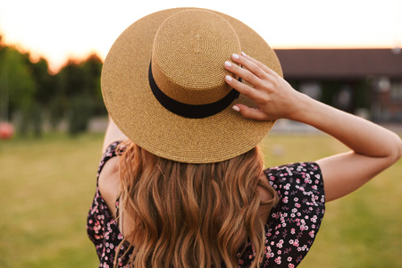 Portrait from back of european woman 20s wearing straw hat and dress walking outdoor on nature in...
