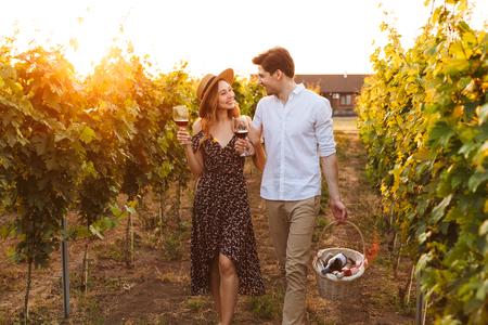 Photo of young cute happy loving couple outdoors drinking wine holding basket with bottles.の写真素材