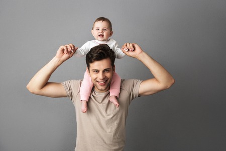 Portrait of a cheerful young father holding his little baby girl over gray background, playingの写真素材