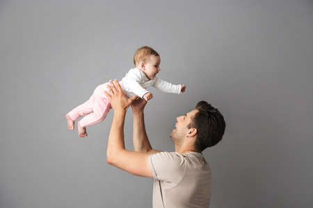 Image of caucasian father man holding his little baby in hands isolated over gray backgroundの写真素材