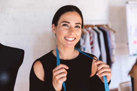 Smiling young woman tailor with measuring tape at the studio