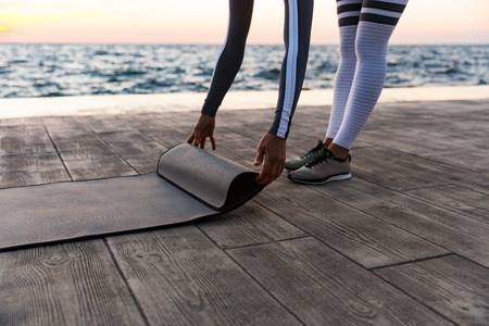Cropped image of a young woman unrolling fitness mat at the beachの写真素材