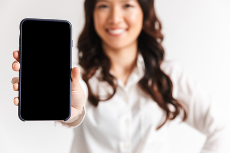 Close up of a smiling asian businesswoman showing blank screen mobile phone isolatedの写真素材