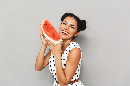 Portrait of a cheerful young woman in summer dress isolated, holding watermelon sliceの写真素材